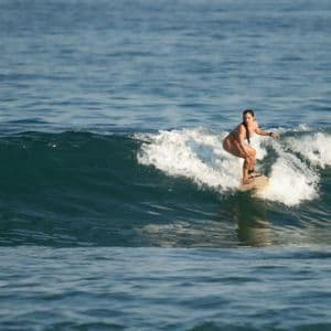Una donna in bikini in equilibrio su una tavola da surf, cavalca un'onda nell'oceano aperto di giorno.