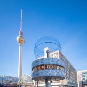 Un gran reloj mundial en una plaza de la ciudad, con una alta torre de televisión al fondo bajo un cielo azul claro.