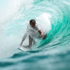 Un surfista con lunghi capelli cavalca la tavola da surf all'interno del tubo di una grande onda turchese che si arriccia.