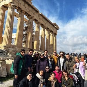A WeRoad group trip posing for a photo in front of a large classical temple with stone columns under a blue sky.
