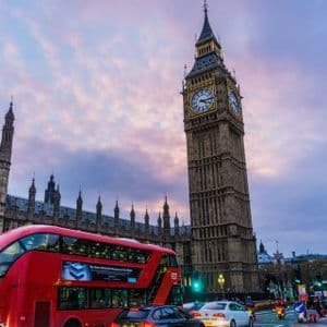 Un bus rouge à impériale passe devant la tour de l'horloge de Big Ben et le Parlement sous un ciel nuageux au crépuscule.