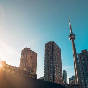 Vue en contre-plongée d'une ligne d'horizon urbaine, avec une tour d'observation et des gratte-ciel, sous un ciel bleu clair avec un reflet solaire.