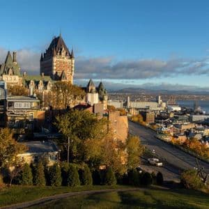 Un paysage urbain avec un bâtiment historique ressemblant à un château, des arbres d'automne et un port fluvial avec des navires de croisière amarrés.