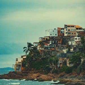 Un pueblo de edificios coloridos se asienta en una ladera rocosa y costera con palmeras y las olas del mar abajo.