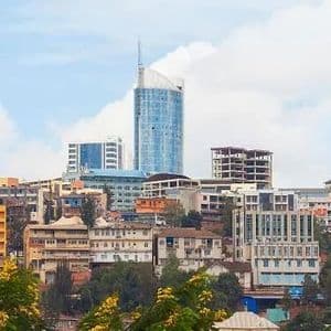 Un paysage urbain dense avec un gratte-ciel moderne en verre et d'autres bâtiments sur une colline sous un ciel partiellement nuageux.