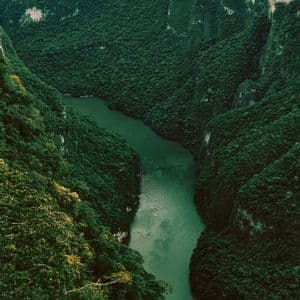 Vista aerea di un fiume verde che serpeggia in un profondo canyon con pendii scoscesi coperti da fitta foresta.