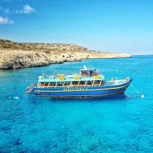Voyage en groupe WeRoad sur un bateau ancré dans une eau turquoise, avec des nageurs près d'une côte rocheuse.