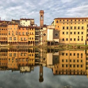 Una hilera de coloridos edificios ribereños y un campanario que proyecta un claro reflejo en las tranquilas aguas.
