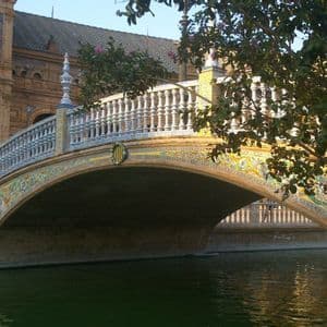 Un ponte ad arco decorato con piastrelle colorate e una balaustra bianca attraversa un canale di fronte a un grande edificio in mattoni.