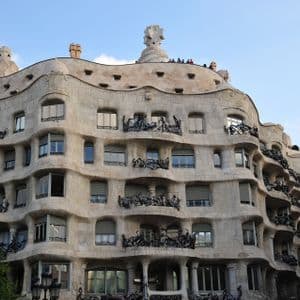 Un edificio in pietra ondulato con balconi in ferro battuto ornati e comignoli scultorei sul tetto, visto contro un cielo azzurro.