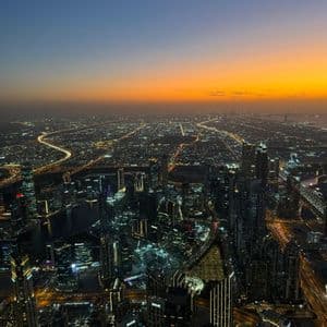 Veduta aerea di una metropoli estesa al crepuscolo, con grattacieli e autostrade illuminati sotto un cielo sfumato arancione e blu.