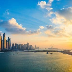 Una vista aerea dello skyline di una città moderna con grattacieli in riva al mare, illuminata da un tramonto dorato.