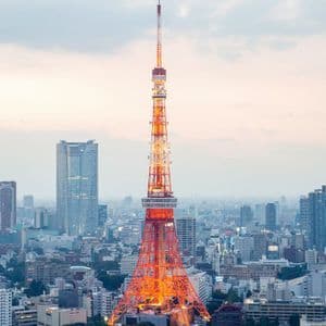 Una torre reticolare illuminata rossa e bianca si erge imponente tra un vasto skyline cittadino ricco di edifici moderni sotto un cielo nuvoloso.