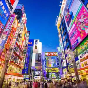 Una trafficata strada cittadina al tramonto è affiancata da alti edifici coperti da luminosi e colorati cartelloni e pubblicità giapponesi.