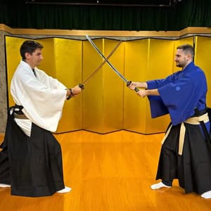 Due uomini in abiti tradizionali giapponesi duellano con le katane, le spade incrociate davanti a un paravento dorato.