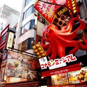 Una grande scultura di polpo rosso su una facciata di edificio, circondata da molti cartelli colorati con caratteri giapponesi su una strada cittadina.