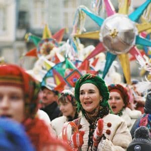 Una folla di persone in abiti tradizionali colorati partecipa a una sfilata di strada, tenendo in mano grandi stelle decorative.