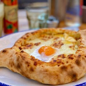 Primo piano di un Khachapuri Adjaruli, un pane a forma di barca ripieno di formaggio fuso e un tuorlo d'uovo crudo, su un piatto.