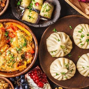 Una vista dall'alto di un ricco assortimento di piatti tradizionali, tra cui ravioli, stufati, insalate, formaggi e frutta fresca, disposti su una superficie scura.