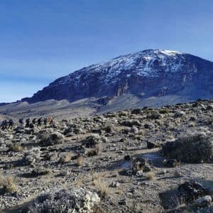 Un gruppo WeRoad in viaggio fa trekking in fila attraverso un paesaggio roccioso e d'alta quota, con un'imponente montagna innevata in lontananza.