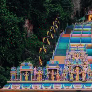 Una lunga e colorata scalinata conduce su un ripido pendio ricoperto di giungla verso l'ingresso di un tempio ornato.