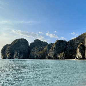 Grandi scogliere rocciose coperte di vegetazione emergono dalle acque calme e turchesi di una baia sotto un cielo azzurro e limpido.