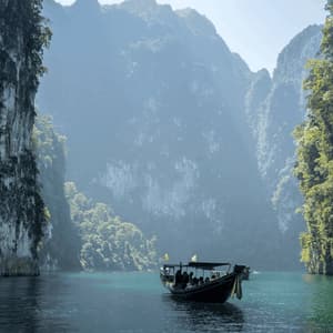 Un viaggio di gruppo WeRoad su una long-tail boat galleggia su acque calme tra imponenti scogliere calcaree coperte da una vegetazione lussureggiante.