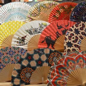 Un assortimento di ventagli spagnoli colorati e decorati, con stecche di legno, esposti a file sovrapposte su una bancarella del mercato.