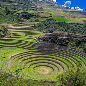 Concentric circular agricultural terraces with stone walls built into a lush green hillside under a blue sky.