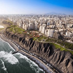 An aerial view of a coastal city built on steep cliffs, with a highway below and waves crashing on the beach.