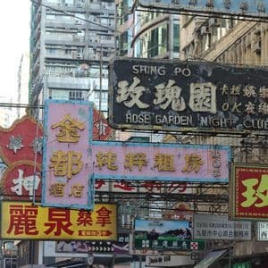 Un fitto gruppo di insegne logore con caratteri cinesi pende su una strada urbana davanti a edifici alti.