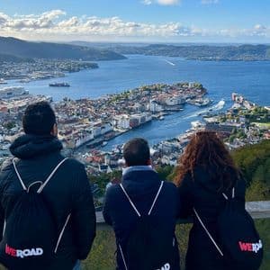 Un viaggio di gruppo WeRoad di tre persone viste di spalle, che osservano una città costiera e un porto da un punto panoramico.