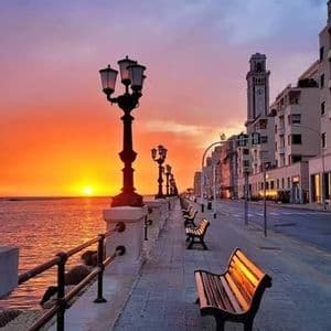 Una passeggiata sul lungomare con panchine e lampioni al tramonto sul mare.