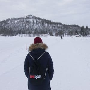 Una persona di un viaggio di gruppo WeRoad, vista da dietro, cammina attraverso un vasto paesaggio innevato con una collina boscosa sullo sfondo.