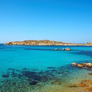 Una baia costiera con acqua cristallina turchese, una costa rocciosa e una piccola barca che galleggia sotto un cielo blu.
