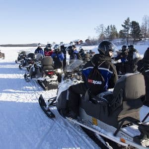 Un viaggio di gruppo WeRoad, con caschi e abbigliamento invernale, pronti a sfrecciare su motoslitte allineate in un paesaggio innevato.