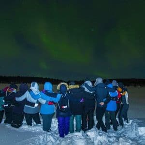 Un gruppo WeRoad, compatto nella neve, ammira l'aurora boreale verde nel cielo notturno.