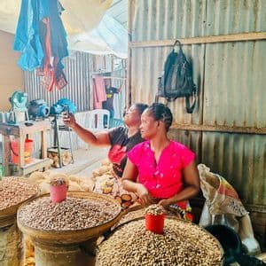 Una donna si fa un selfie con un'altra donna a una bancarella del mercato che vende grandi cesti di arachidi.