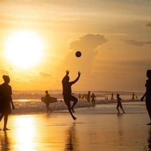 Un gruppo WeRoad in silhouette su una spiaggia al tramonto, con una persona che salta per afferrare una palla.