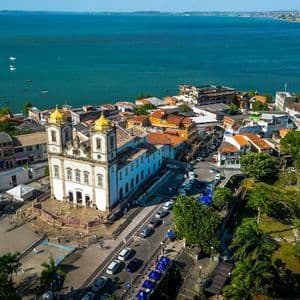 Vista aerea di una storica chiesa bianca con doppie cupole dorate che domina una città costiera e una baia con barche.