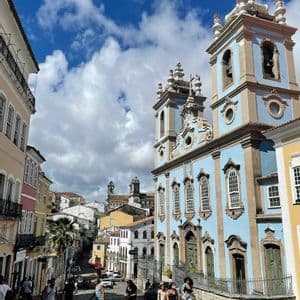 Un viaggio di gruppo WeRoad percorre una strada acciottolata, accanto a una storica chiesa azzurra con due campanili, sotto un cielo blu con nuvole bianche.