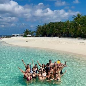 Un gruppo WeRoad in posa e sorridente in acque basse e turchesi, vicino a una spiaggia di sabbia bianca orlata di palme.
