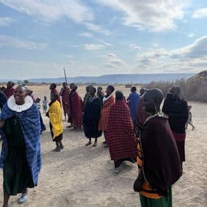 Un gruppo di Maasai, con indosso colorate vesti tradizionali e gioielli, si riunisce nel loro villaggio in un paesaggio arido e aperto.
