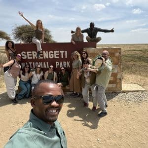 Un viaggio di gruppo WeRoad in posa per un selfie davanti al cartello del Parco Nazionale del Serengeti in una giornata di sole.