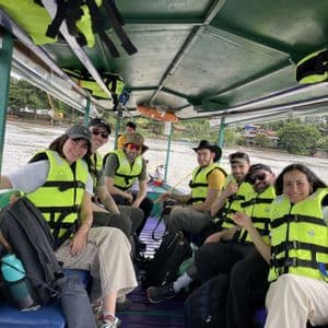 Gruppo WeRoad sorridente in barca sul fiume con giubbotti di salvataggio gialli.