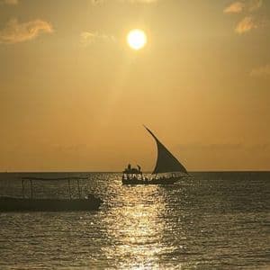 Un viaggio di gruppo WeRoad su un tradizionale dhow, la cui sagoma si staglia sull'oceano contro un tramonto dorato.
