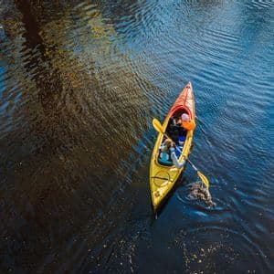 Luftaufnahme: Zwei Personen paddeln ein gelbes Kajak auf dunklem, gewelltem Wasser.