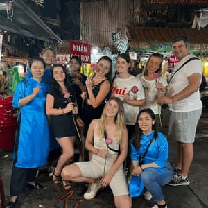 A WeRoad group trip poses for a photo at a bustling night market, with several members holding pink lotus flowers.