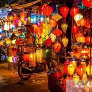 Una bancarella del mercato notturno piena di dozzine di lanterne colorate e luminose di varie forme, con una bicicletta parcheggiata davanti.