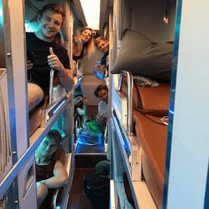 Un gruppo WeRoad in viaggio sorride e posa per la fotocamera dalle proprie capsule letto individuali all'interno di un moderno autobus notturno.